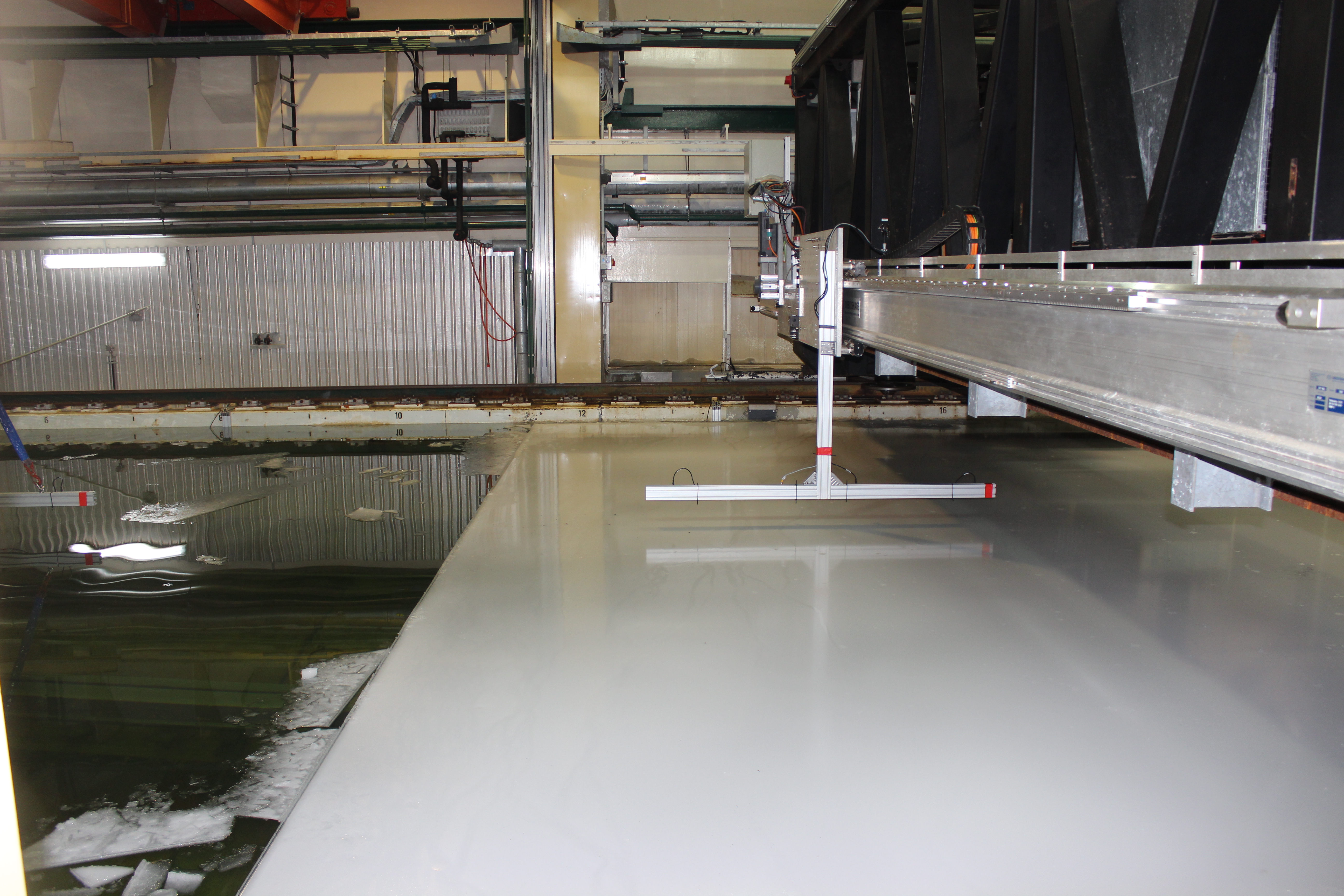 Laboratory investigations of the bending rheology of floating saline ice and wave damping in the HSVA ice tank